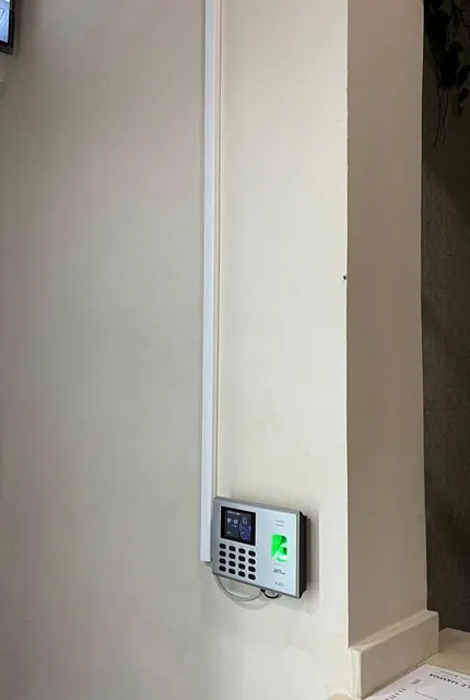 Pointeuse à empreinte fixée sur un angle de mur, câble protégé sous goulotte.
